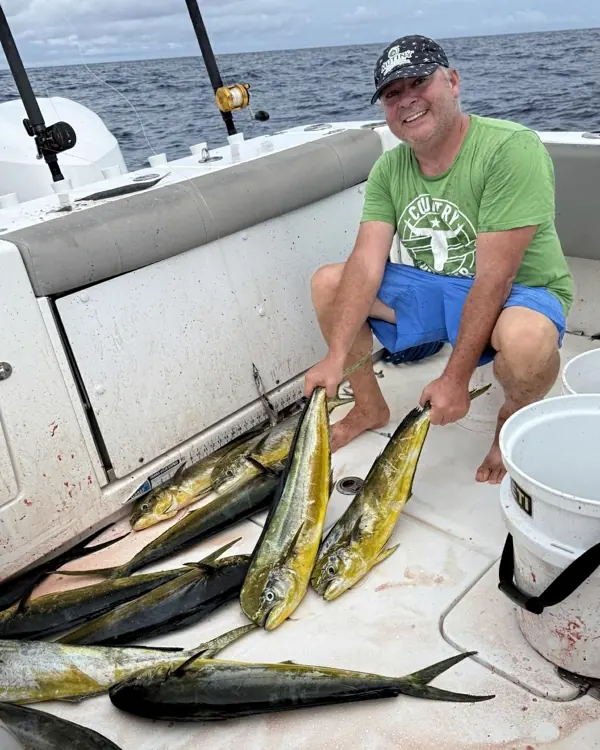 Angler kneeling on deck with several mahi