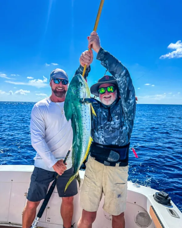 Two anglers holding up a mahi on a boat