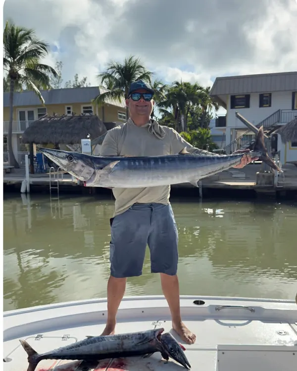 Angler holding a wahoo on a boat by a dock