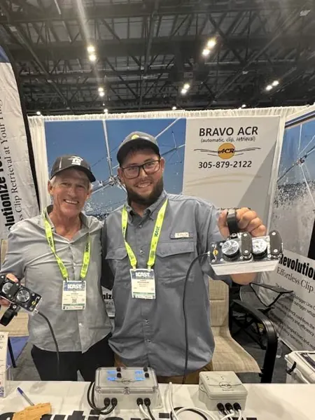 Two men at the Bravo ACR booth holding a handheld unit and a white Bravo ACR box